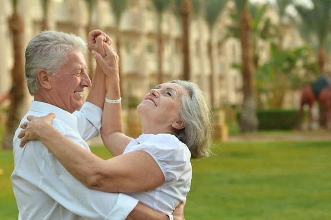 Happy retired couple dancing, palm trees in background